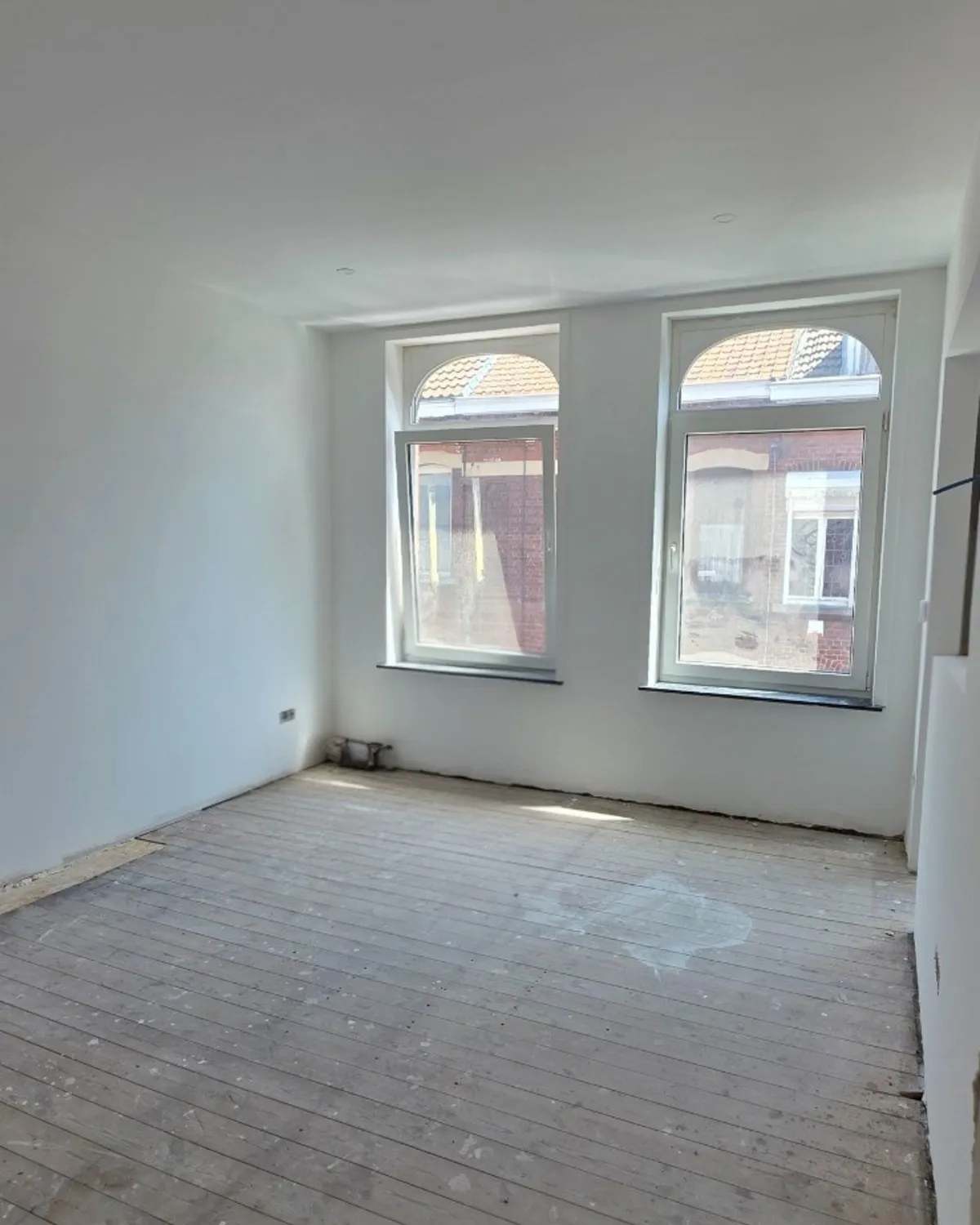 Pièce avant travaux : deux fenêtres cintrées, plancher d'origine et murs fraîchement enduits.